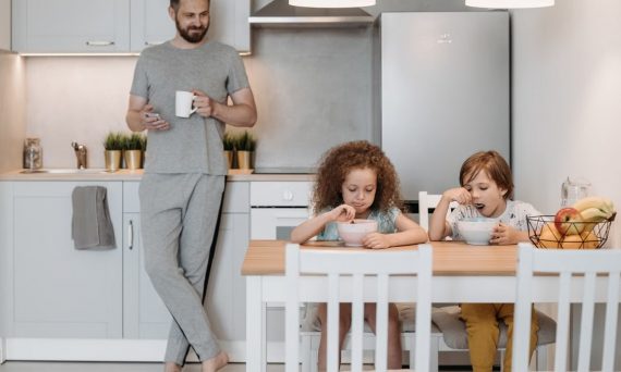 A father with two children enjoying breakfast in a bright, modern kitchen at home.